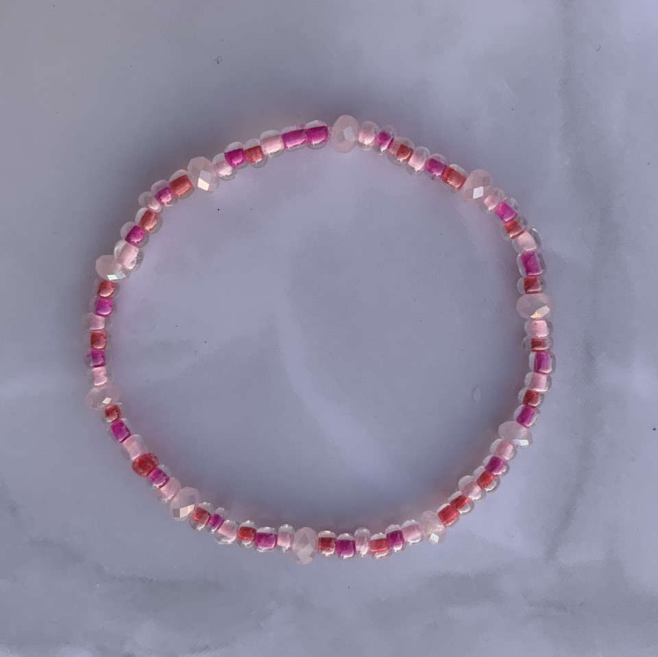Håndlaget strikkarmbånd med vakre små cerise og rosafargede perler. Et nydelig og enkelt armbånd som med fordel kan kombineres med andre favorittarmbånd. Elastisk strikk for optimal passform. Både de små runde og fasetterte perlene er laget av glass.