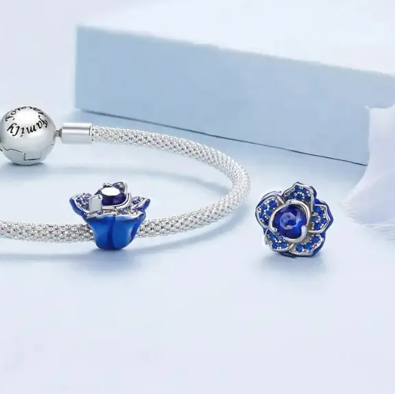 NÆRBILD AV JBX CHARM BLUE FLOWER SILVER PÅ ET ARMBÅND OG ALENE
